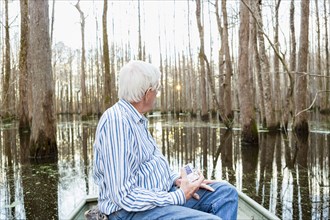 Older Caucasian man riding boat in swamp