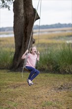 Caucasian girl playing on swing in field