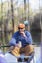Caucasian man drinking beer in canoe on river