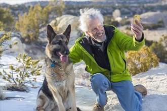 Older man taking cell phone photograph with dog on rock formations