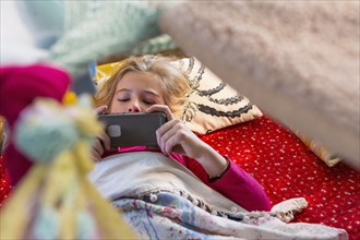 Caucasian girl using cell phone in blanket fort