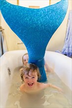 Caucasian children playing with mermaid tail in bath