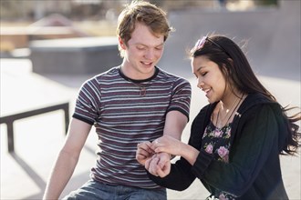 Teenage girl tying bracelet around wrist of boyfriend