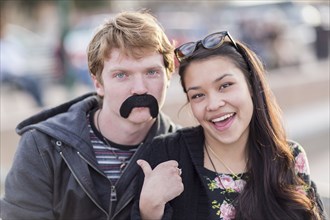 Teenage couple playing with fake mustache