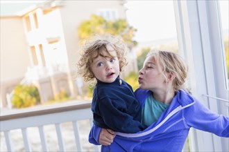 Caucasian girl carrying baby brother on porch