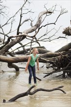 Caucasian girl playing in river near driftwood