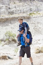 Caucasian father carrying son on shoulders on dirt path