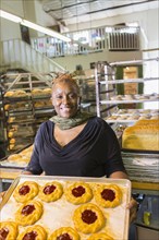 Black baker holding tray of pastries in bakery kitchen