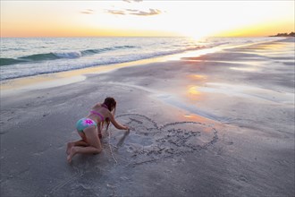 Caucasian girl drawing in sand on beach