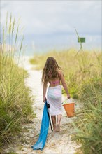Caucasian girl carrying pail and towel on beach