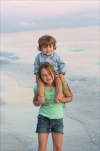 Caucasian girl carrying brother on shoulders on beach