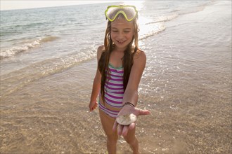 Caucasian girl holding sand dollar on beach