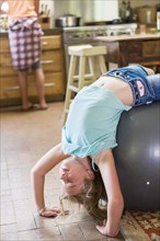 Caucasian girl playing on exercise ball in kitchen