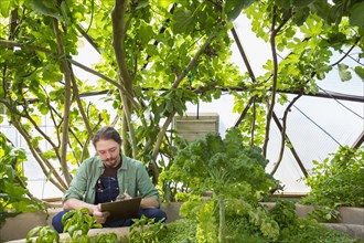 Caucasian gardener writing on clipboard in greenhouse