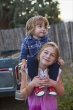 Caucasian girl carrying brother on shoulders