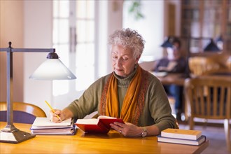 Older mixed race woman reading book in library