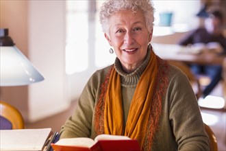 Older mixed race woman holding book in library