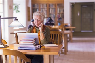 Older mixed race woman using laptop in library