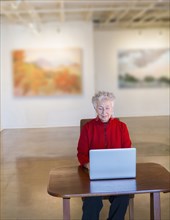 Older mixed race woman using laptop in art gallery