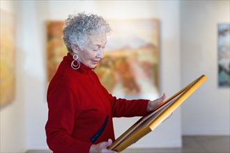 Older mixed race woman holding picture in art gallery