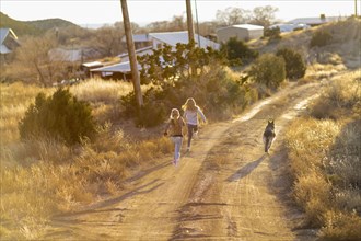 Caucasian children running on dirt road with dog