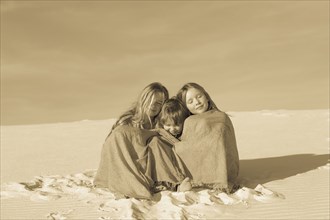 Caucasian children wrapped in blankets in desert