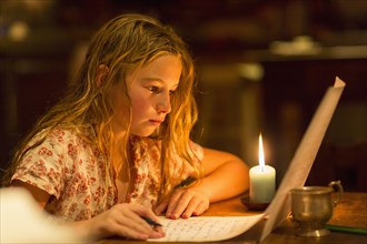 Caucasian girl writing by candle light