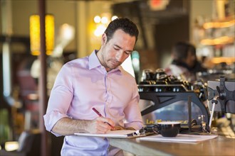 Hispanic businessman writing on clipboard in coffee shop