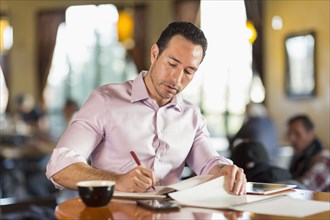 Hispanic businessman writing in coffee shop
