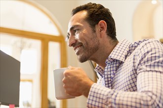 Hispanic businessman drinking coffee in office