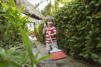 Caucasian boy playing with broom on path near house