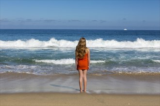 Caucasian girl standing looking at ocean waves