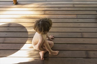 Naked Caucasian boy sitting on wooden deck