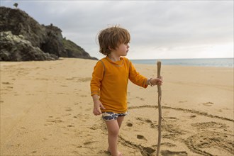 Caucasian boy with walking stick on beach