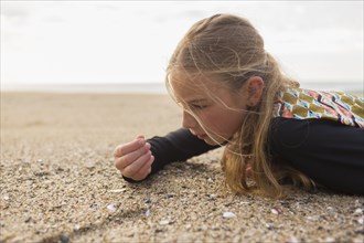 Caucasian girl laying on beach examining seashells