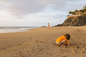 Caucasian boy digging in sand on beach