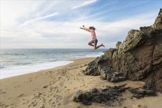 Caucasian girl jumping off rocks at beach