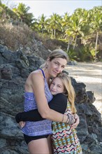 Caucasian mother and daughter hugging near rocks at beach