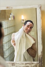 Naked Hispanic man drying with towel in mirror