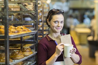 Caucasian woman holding clipboard drinking coffee in bakery