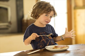 Caucasian boy gesturing while eating pancakes