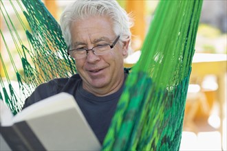 Caucasian man reading book in green hammock