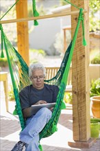 Caucasian man using digital tablet in green hammock