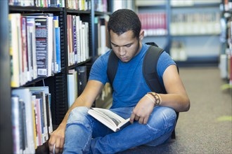 Mixed Race boy sitting on floor reading book in library