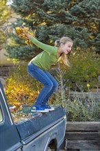 Caucasian girl holding autumn leaves jumping off truck