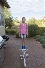 Caucasian girl standing on seat of bicycle