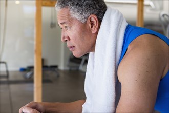 Mixed Race man resting with towel around neck during workout
