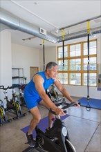 Mixed Race man riding stationary bicycle in gymnasium