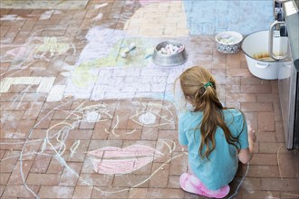 Caucasian girl drawing face with chalk on patio bricks