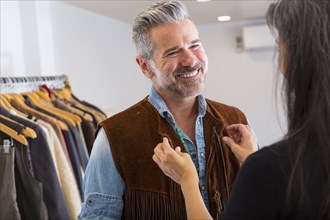 Woman helping man with fringe vest in store